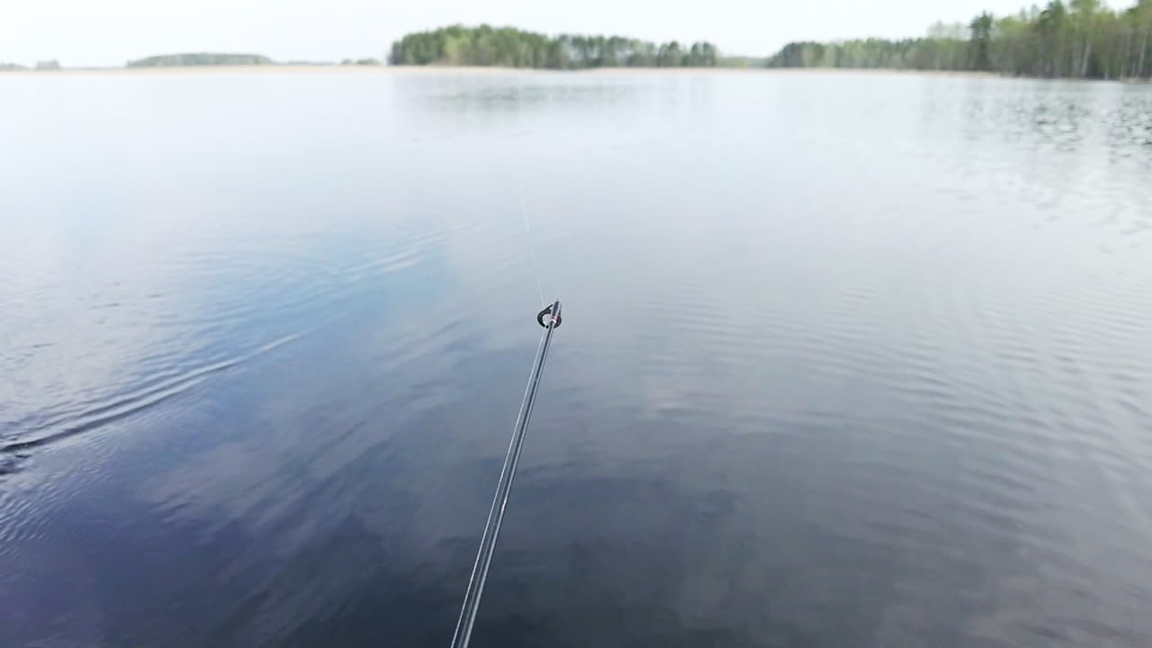 Rekaman gerak lambat ujung joran pancing yang bergoyang saat memancing dengan teknik trolling di danau yang tenang.