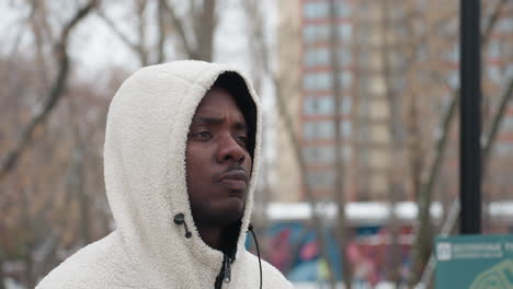 confident man in white hoodie eating while walking, focused expression, blurred winter background featuring bare trees, colorful building, and street sign