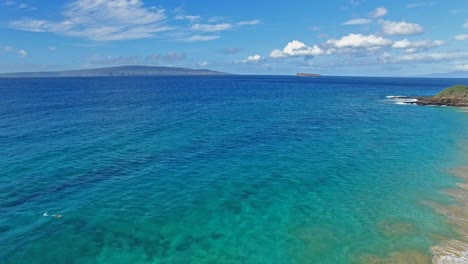 Panning-aerial-shot-of-a-Snorkler-in-Maui-Hawaii-in-beautiful-blue-water-with-sandy-beach-and-land-in-background