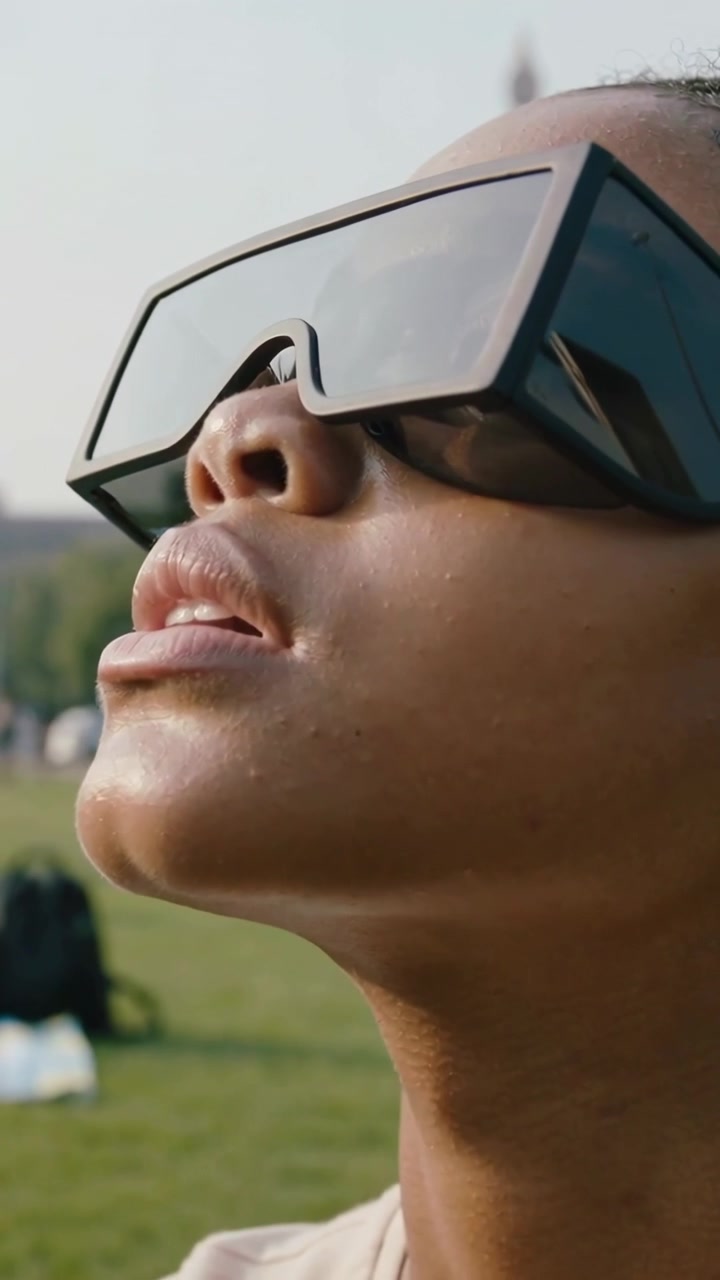 Vertical video: Tilting woman in light top lifting chin in park sensing sun, shades showing spire