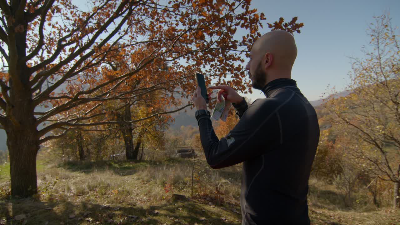 휴대전화를 들고 있는 젊은이가 산에 있는 나무의 사진을 찍고 있는 뒷면. 렌즈 플레어. 은 가을 날