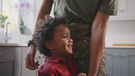 army mother in uniform home on leave playing with son in family kitchen