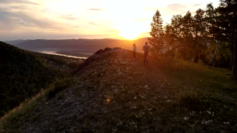 aerial shot of a young couple running to the top of a mountain at sunset.