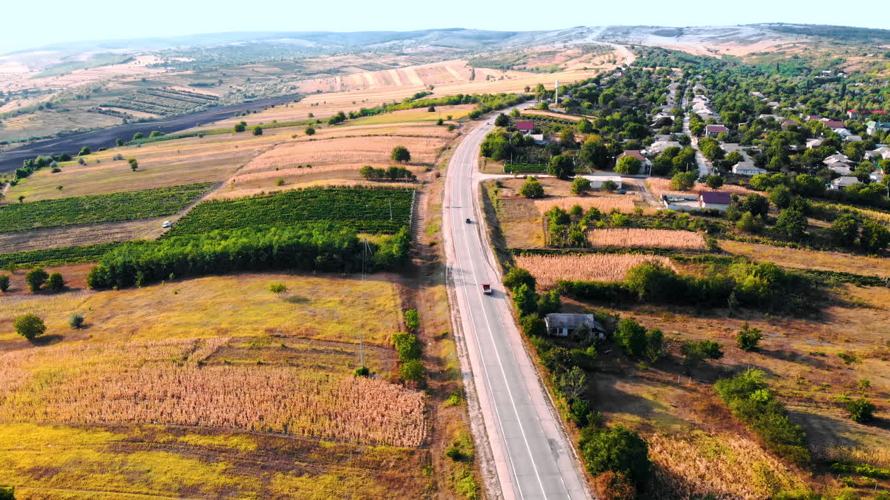 Aerial drone view of a road with moving cars in highland. Small village and green hills on background. Sunny day. Balti, Moldova