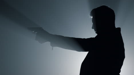 silhouette focused man shooting gun in darkness. criminal aiming with pistol.