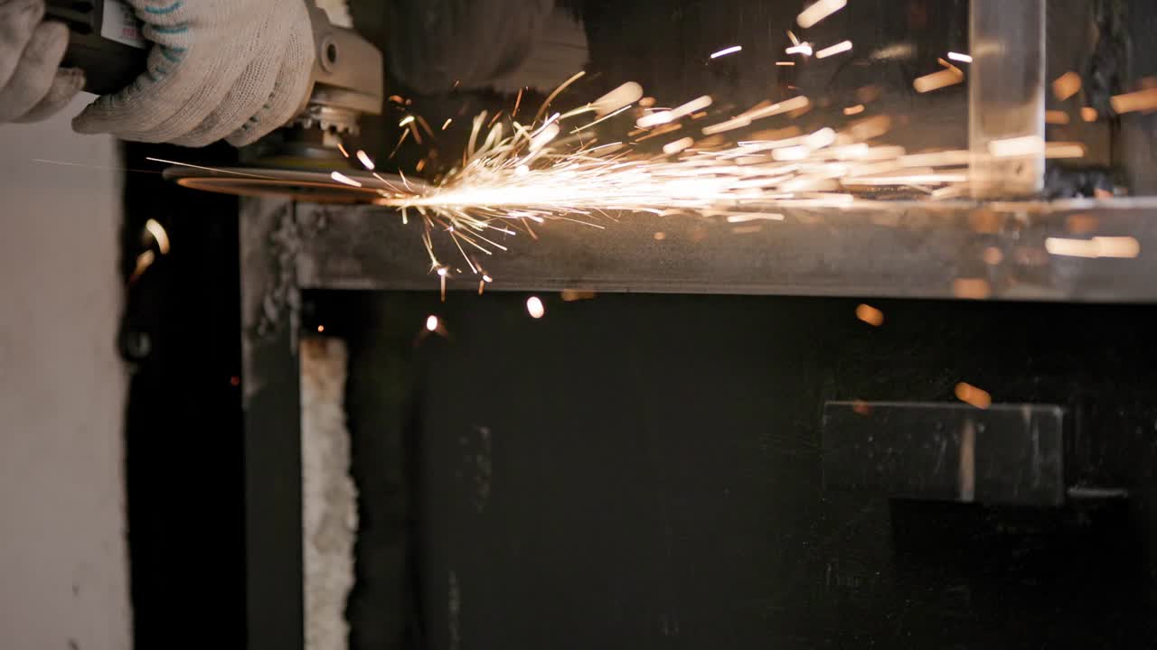 용접 된 금속 구조에서 플래프 디스크를 가진 각 밀러와 함께 용접 된 접합을 수동으로 청소하십시오. 긴 스파크 트레일과 함께 클로즈업, 느린 동작.