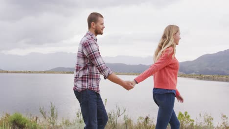 caucasian couple having a good time on a trip to the mountains, walking near lake and holding hands