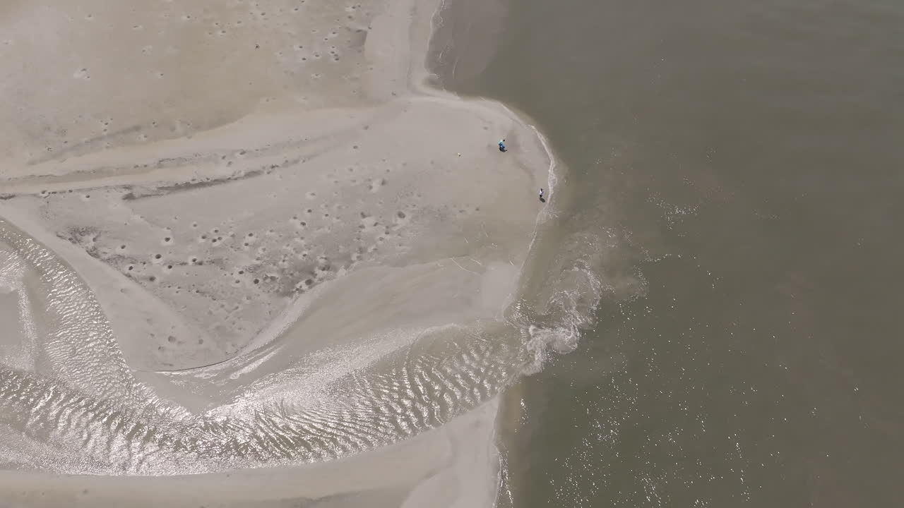 People stand where silver tidewater meets the sea, the tiny figures adding scale to a glowing, fan-like pattern of water on sand