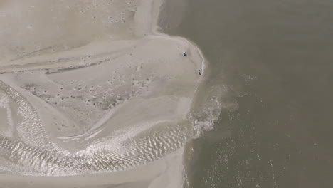 people stand where silver tidewater meets the sea, the tiny figures adding scale to a glowing, fan-like pattern of water on sand