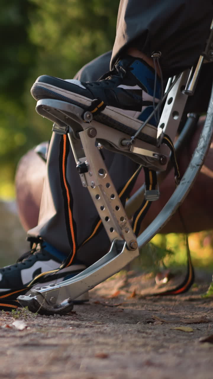 Close-up of young man's legs in dark pants and black and blue sneakers outdoors, focused on handling archery equipment. Bright green surroundings as he works with his gear
