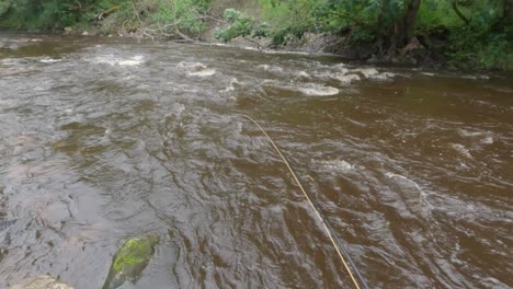 POV-Aufnahme-Einer-Fliegenschnur,-Die-In-Einen-Schnell-Fließenden-Braunen-Fluss-Geworfen-Wird,-Um-Fische-Zu-Fangen