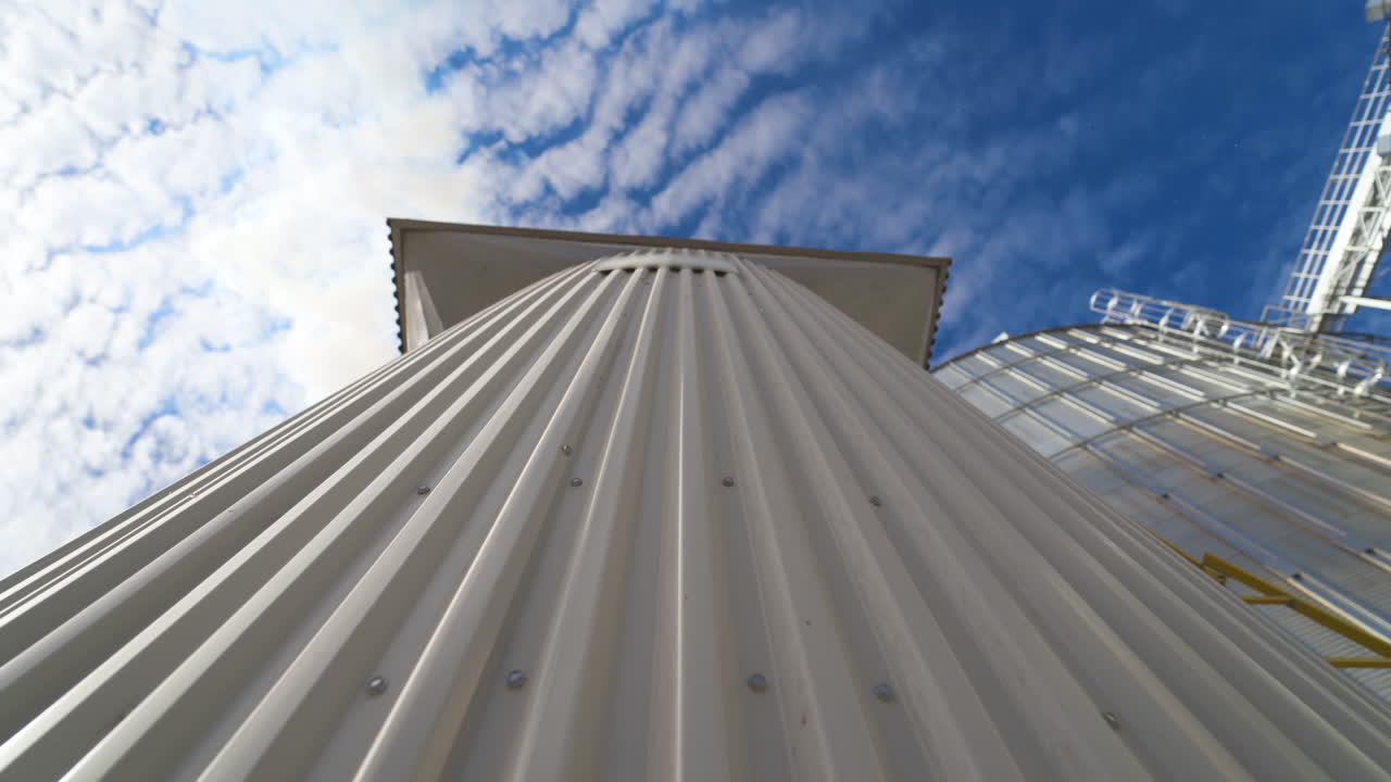 Metal construction on the modern factory. Storage tanks for processing grains on sky background. Smoke releasing from industry into the air. Close-up. Motion camera top down.