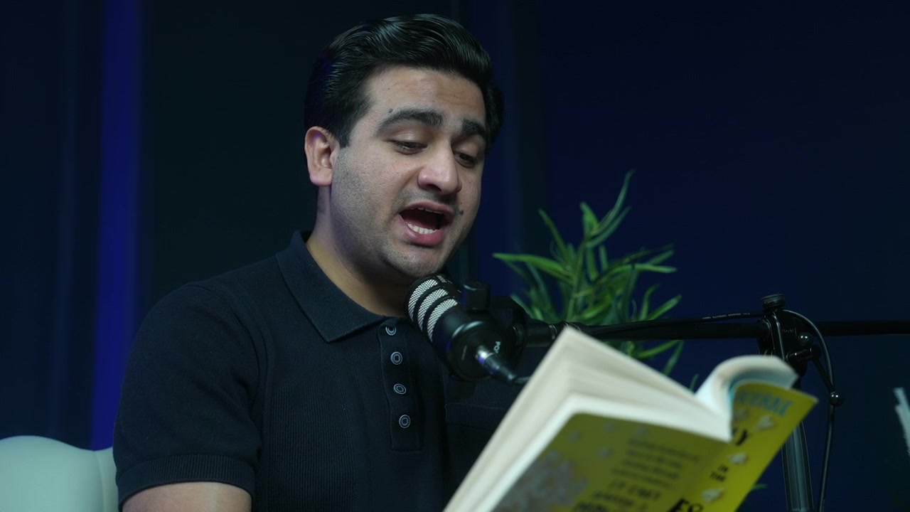 Hombre leyendo un libro en un micrófono en un estudio de podcast con fondo oscuro.