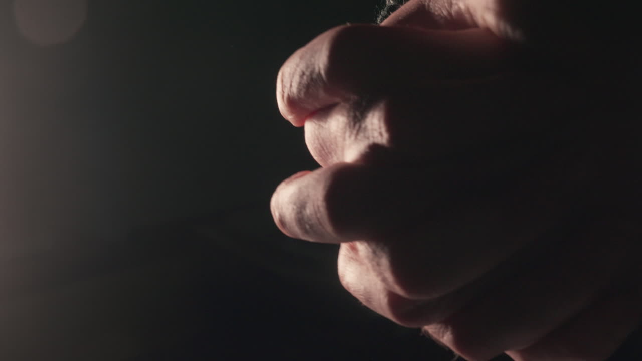 Close-up de mãos apertadas em ambiente com pouca luz. Ideal para temas de tensão, ansiedade, oração e suspense