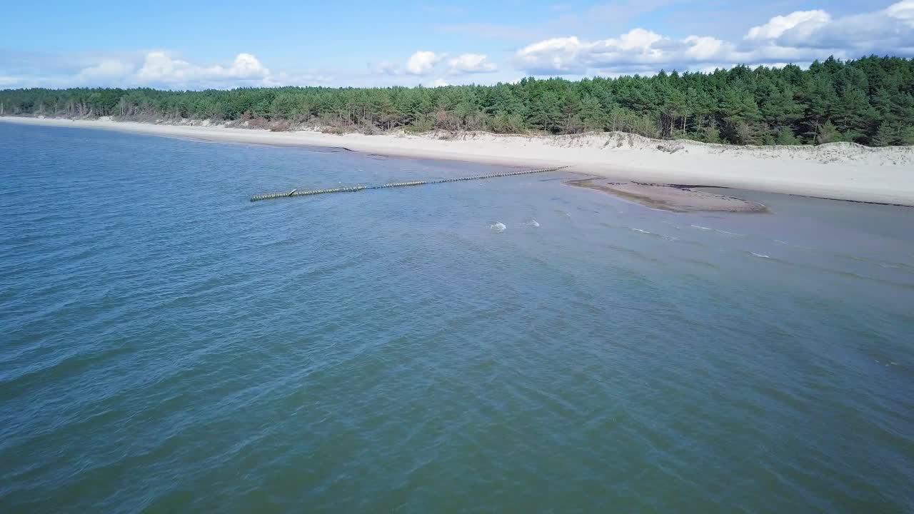 воздушная панорама побережья балтийского моря в солнечный день, дюны на берегу моря, поврежденные волнами, сломанные сосны, старый деревянный пирс, эрозия побережья, изменения климата, широкоугольный снимок с дрона, движущийся вперед