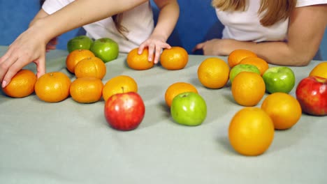 fresh organic fruits on the table. woman and a little girl playing with tangerines and apples on white background. close-up.