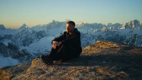 man sitting on mountain top at sunset