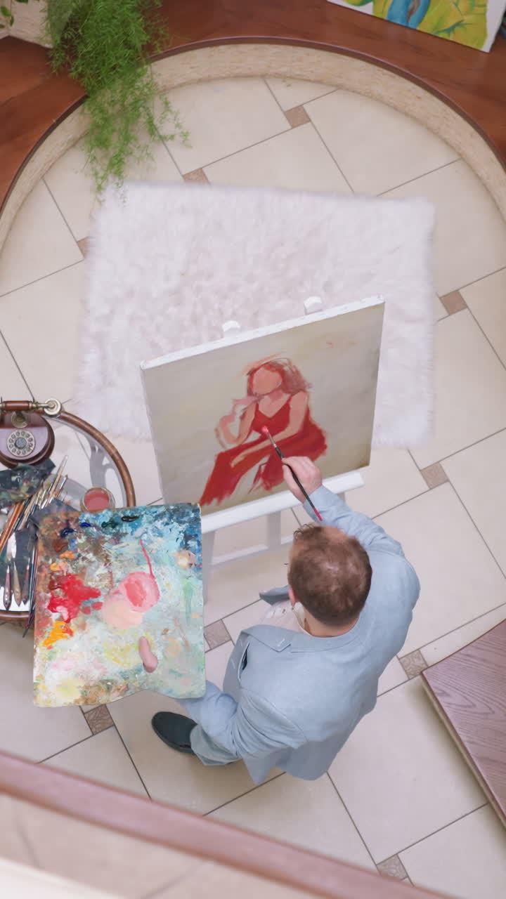 Kunstenaar schildert een dame in het rood aan een ezel. Een getalenteerde meester brengt kleur aan op het elegante damesportret terwijl het model poseert in de galerie. De kunstenaar creëert een portret.