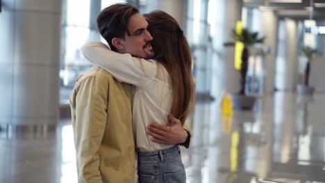 Excited,-woman-showing-passport-with-visa-stamp-to-her-boyfriend-at-the-airport.-Happy-couple,-man-hugging-his-girlfriend-and