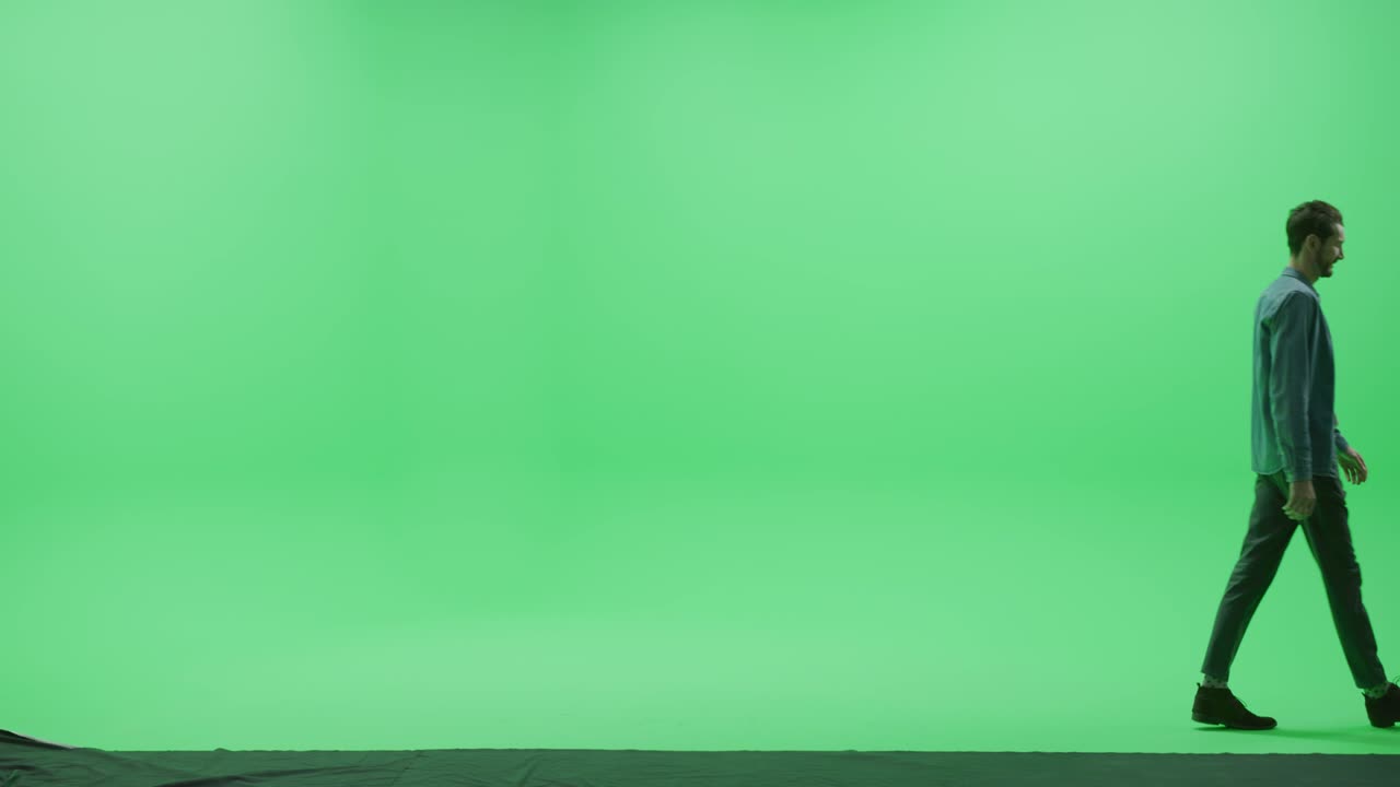 tela verde chroma chave estúdio: forte homem sorridente bonito vestindo roupas casuais caminha através da sala da esquerda para a direita. câmera de visão lateral filmado