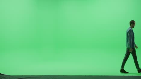 pantalla verde chroma clave estudio: hombre fuerte guapo sonriente con ropa casual camina a través de la habitación de izquierda a derecha. vista lateral disparado por la cámara