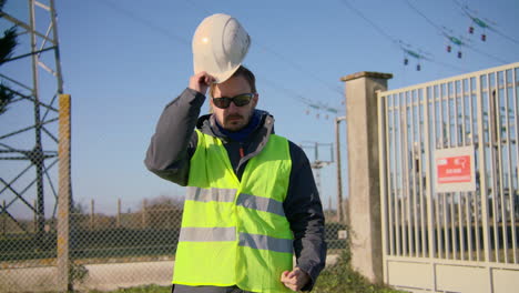 male engineer closing his jacket zipper, wears hard hat, and crossing his arms at the electric substation, handheld