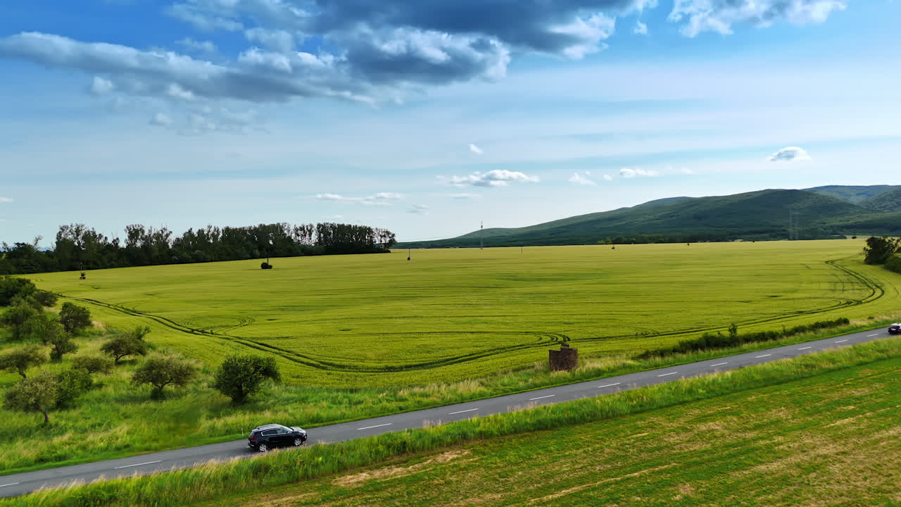 Vast green fields under a bright sky. A wide view of lush green fields stretches across the landscape with hills in the background and clouds overhead