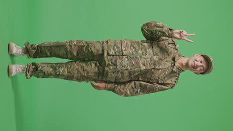 full body of asian man soldier smiling and showing peace gesture to camera while standing in the green screen background studio