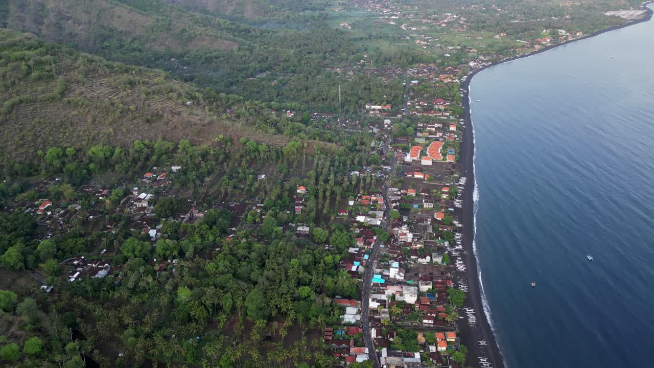 drone vista de arriba hacia abajo de un pequeño pueblo que se extiende a lo largo de la costa con playas de arena negra y volcán en el fondo