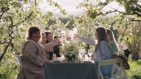 las amigas están celebrando en el jardín sentadas en la mesa con decoración de flores y gafas de clic