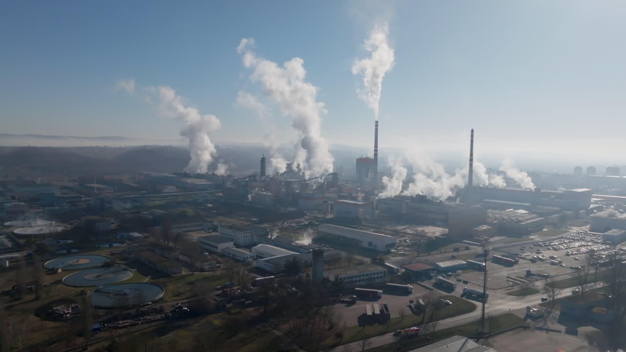 Panorama con drone che cattura lo skyline industriale di Štětí con multiple ciminiere e pennacchi di vapore, più il fiume e il ponte vicini che sfumano nella foschia mattutina