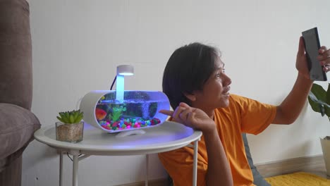 joven asiático graba un video con su pez dorado usando un teléfono inteligente