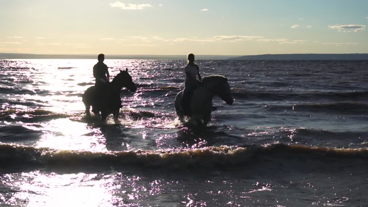 personas a caballo montando en el agua al atardecer