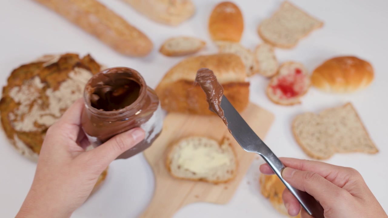 Top-down view of hands using a knife to spread chocolate cream on toast.