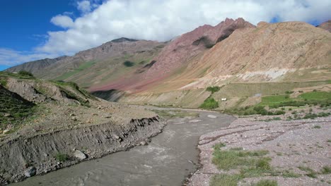 Muddy-brown-river-flowing-through-pin-valley-mountains-in-India-on-sunny-summer-day,-aerial