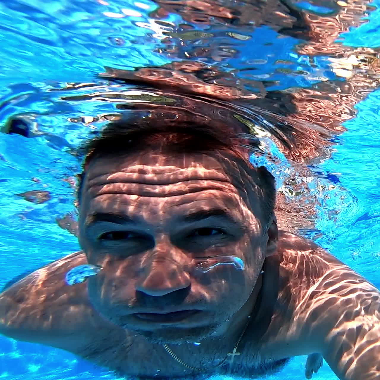 Healthy male is diving in blue water. A man swimming under the clear water with camera inside the pool. Underwater concept.