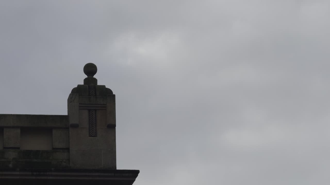 Colonna di pietra con dettagli a croce e sfera in cima, sotto un cielo grigio nuvoloso.
