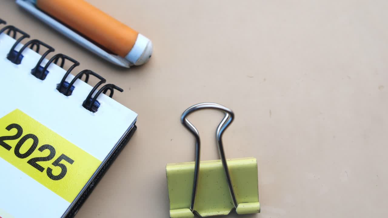 Primo piano di un calendario 2025 su una scrivania con una penna e delle graffette fermacarte.