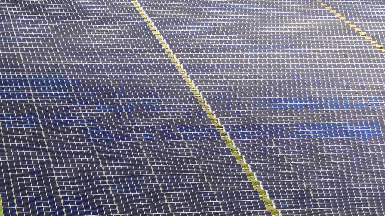 Drone glides above large solar farm, revealing photovoltaic panels in bright, natural daylight