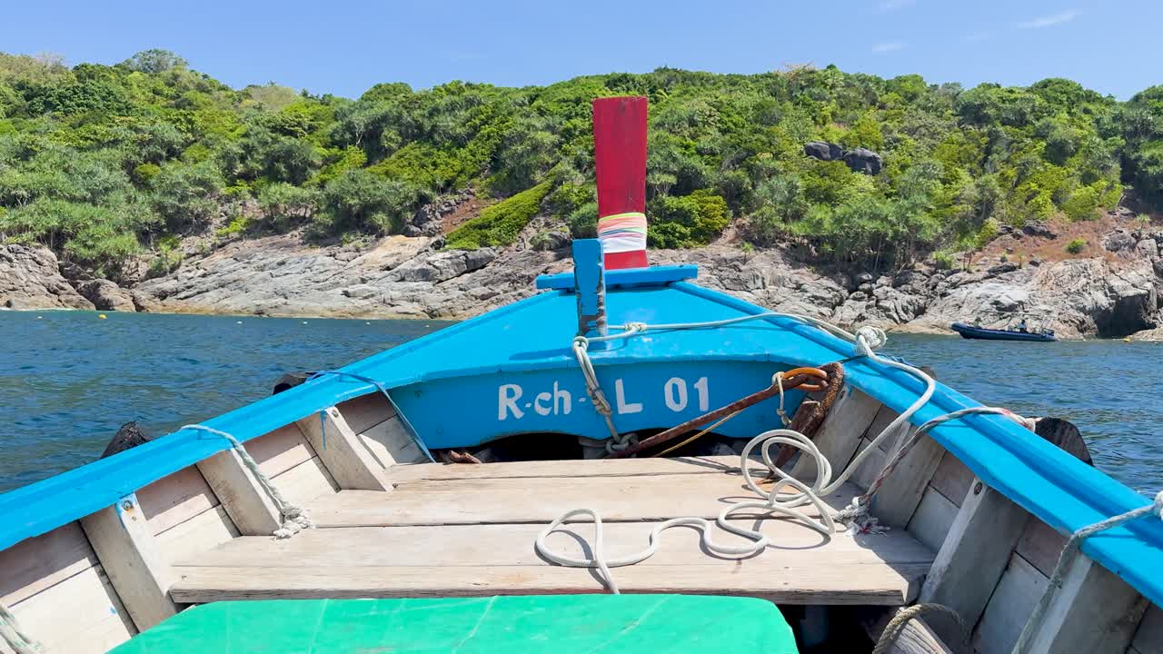 A boat navigates clear waters near a rocky coastline in Phuket, Thailand, under bright daylight, showcasing vibrant colors and serene scenery