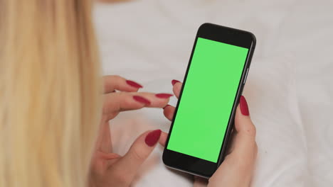 woman using a smartphone with green screen on a bed