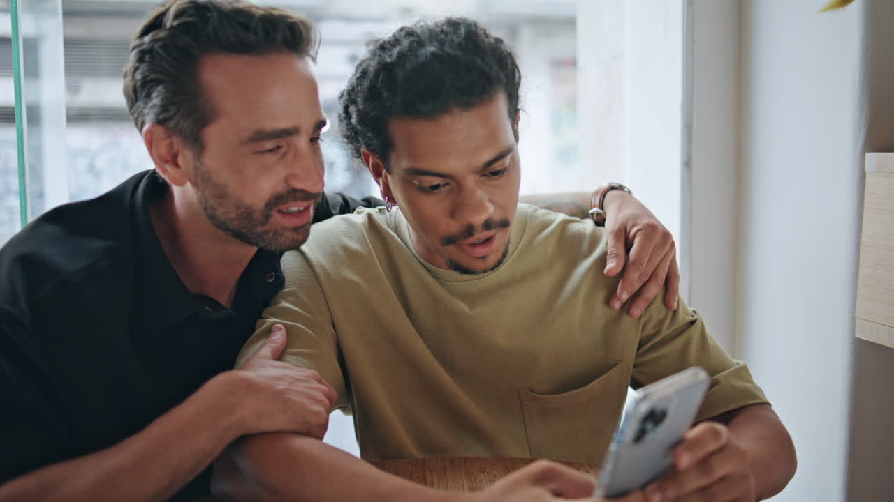 동성 커플이 카페 클로즈업에서 스마트폰 애플리케이션을 스크롤합니다. 사랑스러운 동성애자 남성