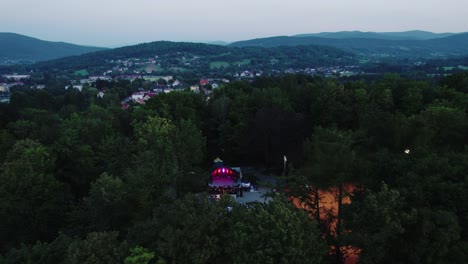 Drohnenaufnahme-Eines-Musikkonzerts-Auf-Der-Beleuchteten-Bühne-Und-Menschenmenge-Im-öffentlichen-Park-Am-Abend