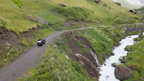 tomada aérea de un coche conduciendo por un camino, un río, un pueblo, montañas, un valle.