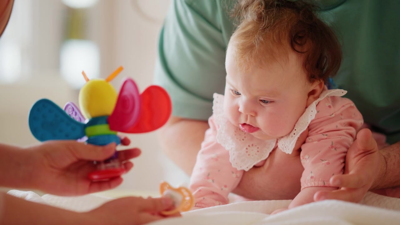 Healthcare professional wearing a medical mask gently supporting a baby during a pediatric care session with a colorful toy nearby