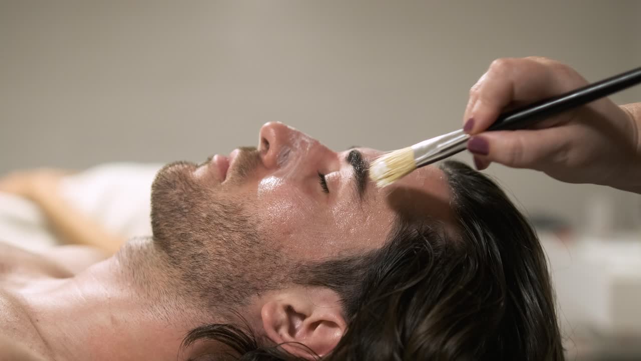 Beautician skillfully applying a rejuvenating face mask to a man