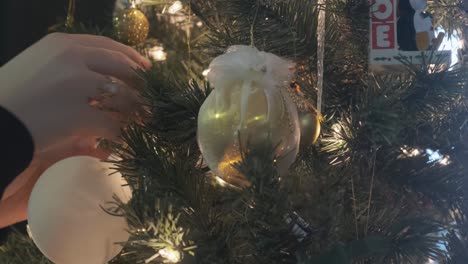 Close-up-shot-of-a-pair-of-hands-placing-a-Christmas-ornament-on-a-beautiful-lit-up-tree