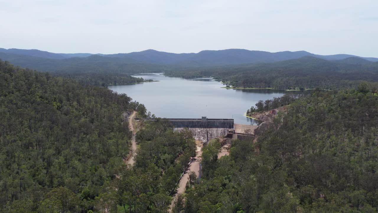 Drone flying towards a dam and a dam wall walking tracks below