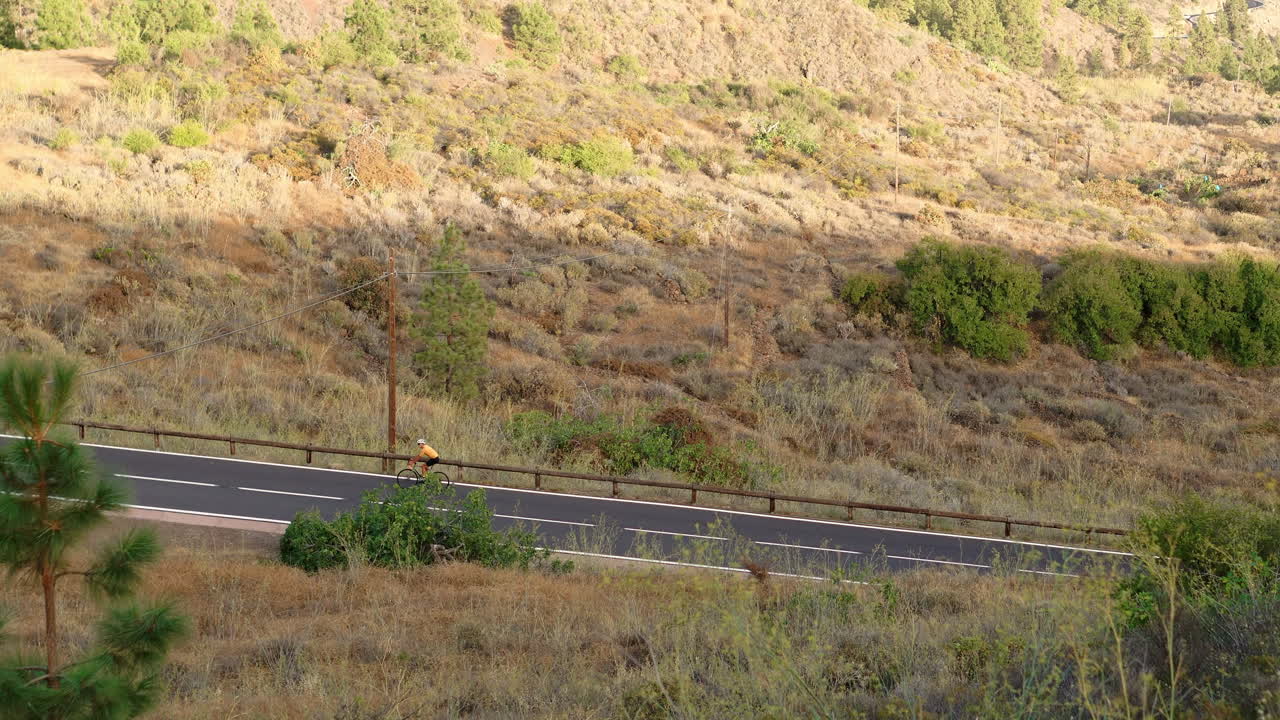 un individuo masculino, vestido con una camiseta amarilla, está en bicicleta encima de una bicicleta de carretera deportiva a lo largo de una carretera ubicada a gran altitud en las montañas