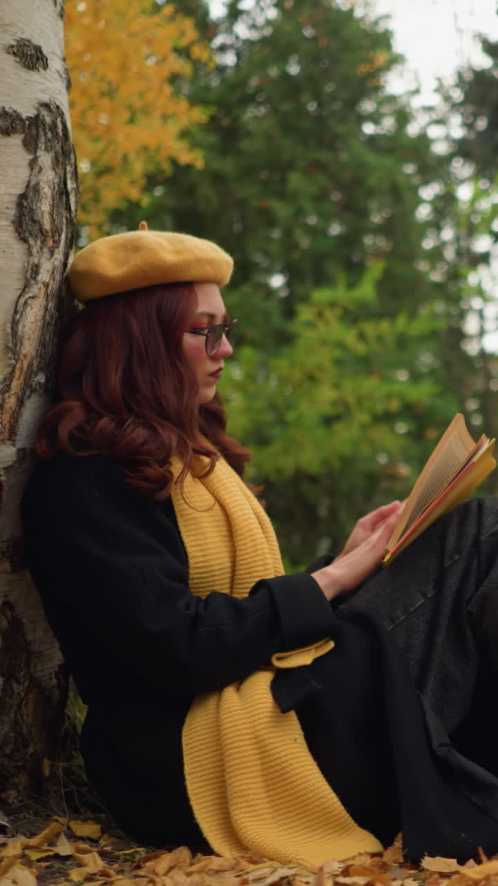 mujer vestida con boina amarilla y bufanda se sienta contra un árbol en el bosque de otoño, repasando pensativamente las páginas de los libros, hojas doradas esparcidas alrededor mejoran la atmósfera pacífica y reflexiva